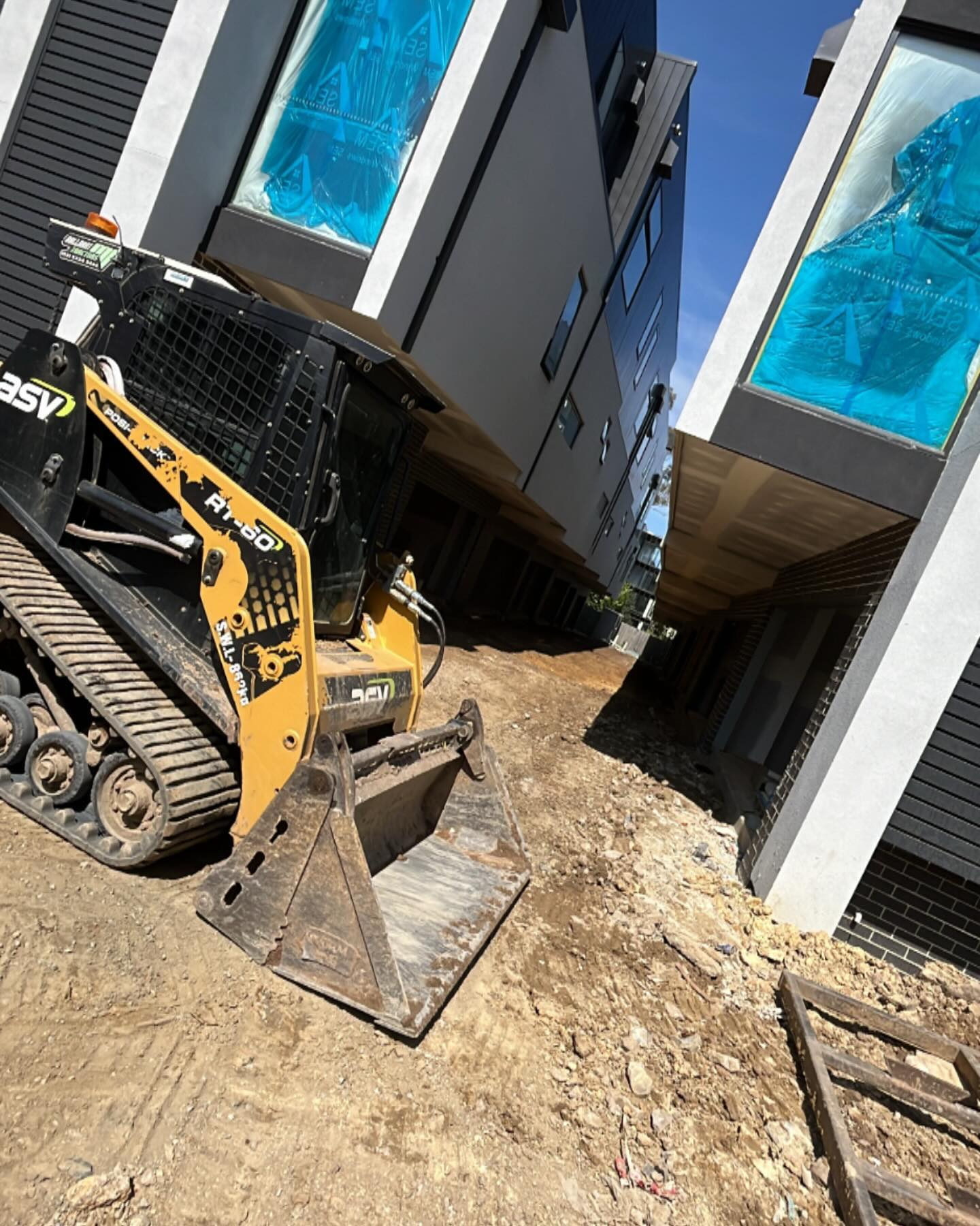 Compact track loader on a dirt site beside new townhouses