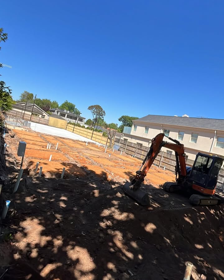 Orange mini excavator on a cleared block with a concrete slab behind