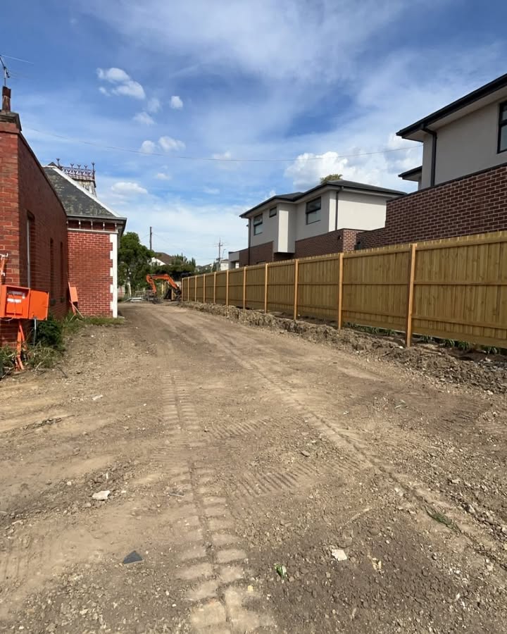 Cleared dirt strip between a brick house and a new timber fence
